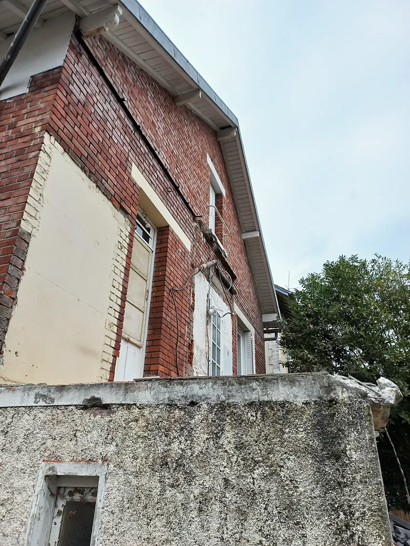Vue en contre-plongée d’une façade en brique percée de portes-fenêtres, garde-corps maçonné en crépi gris au premier plan.