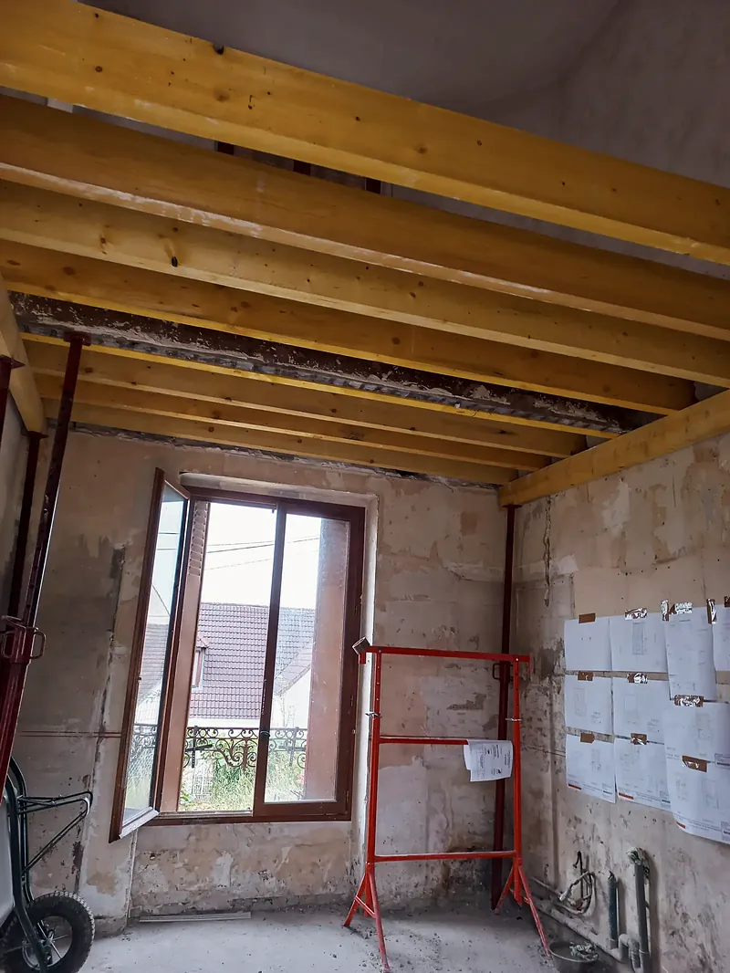 Plafond de solives bois neuves au-dessus d’une pièce en pierre, étais rouges.