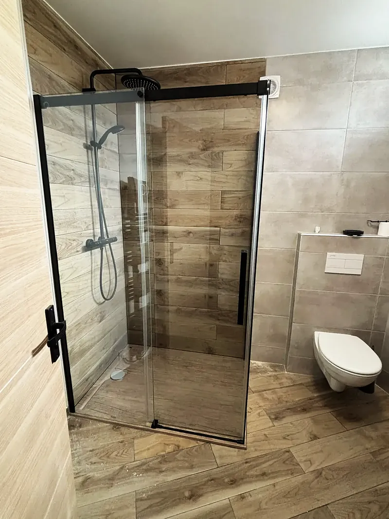 Douche à paroi noire et carrelage effet bois, WC suspendu.