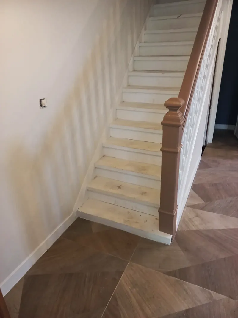 Escalier en bois aux contremarches et balustres blancs, marches en bois clair, main courante et poteau de départ en bois, sol effet bois posé en grands triangles.