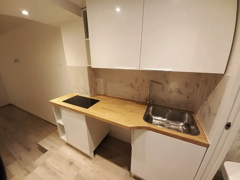 Cuisine blanche avec plan de travail en bois, évier inox, plaque de cuisson et crédence effet marbre.