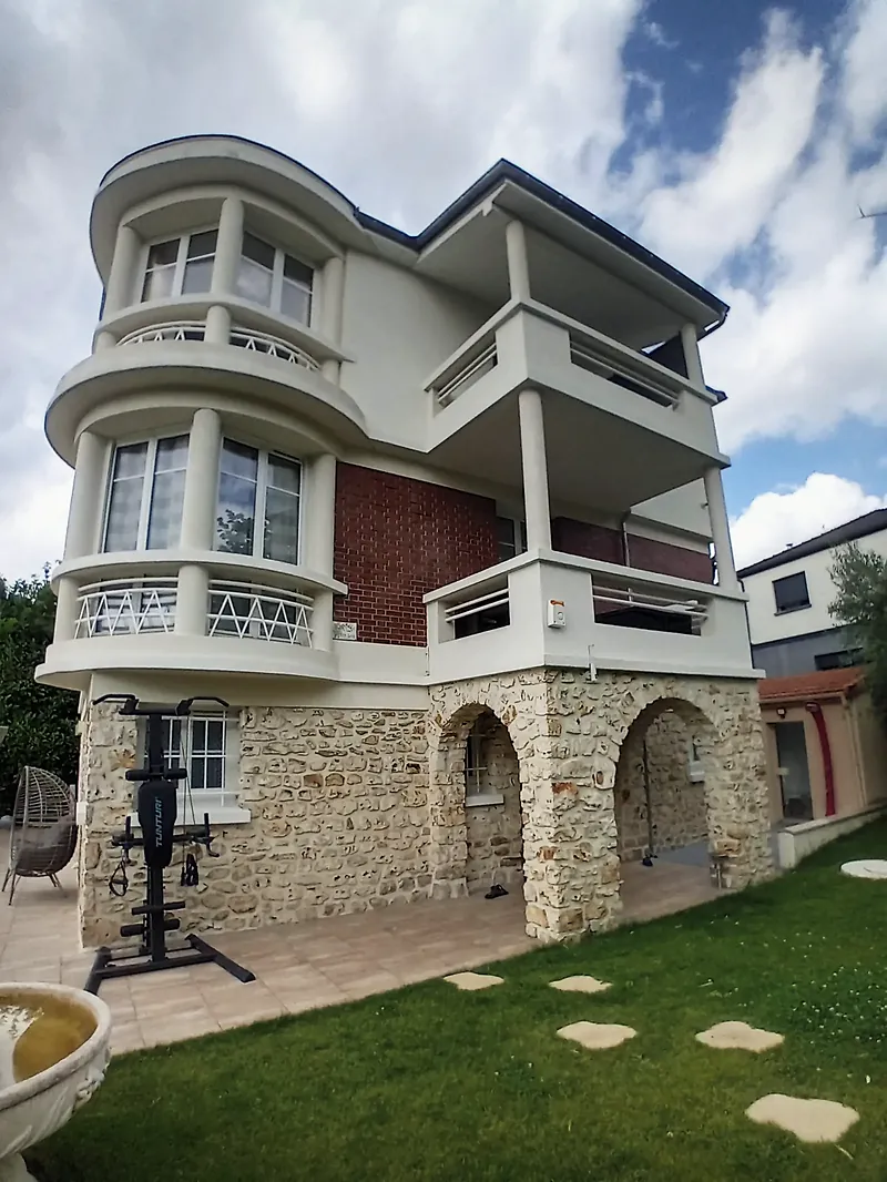 Villa de trois niveaux : soubassement en meulière à arcades, étage en brique rouge, niveau ajouté en enduit clair avec bow-window arrondi et loggia sur colonnes.